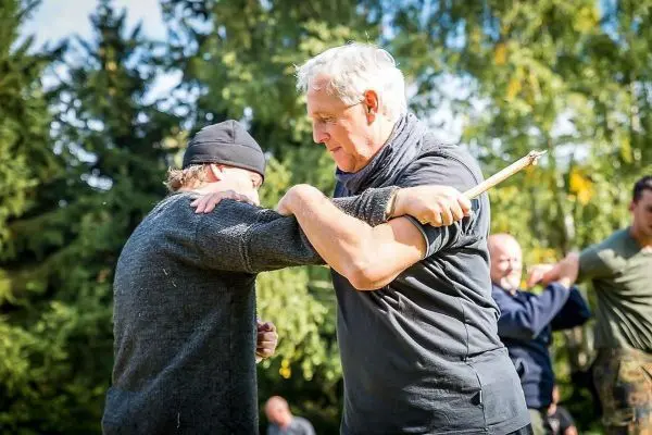Zwei Personen üben einen Nahkampf mit einem Stock in einer Waldumgebung