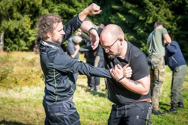 Zwei Personen üben einen Nahkampfgriff im Freien auf einer Wiese