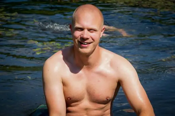 Ein Mann sitzt im Wasser und lächelt, umgeben von Pflanzen