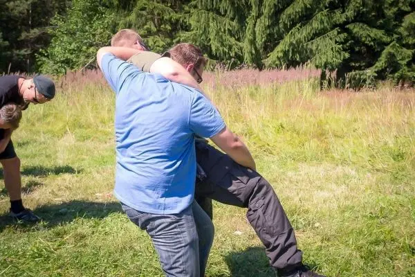 Eine Person trägt eine andere Person über die Schulter in einer Wiese