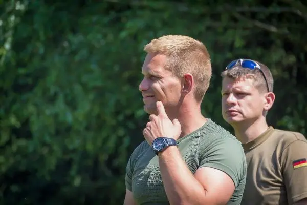 Es sind zwei Männer in militärischer Kleidung zu sehen, einer denkt nach