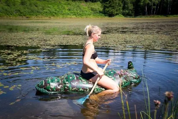 Frau paddelt auf einem camouflagefarbenen Schlauchboot im Wasser