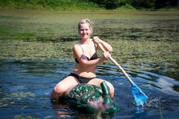 Frau paddelt mit einem blauen Paddel auf einem camouflagefarbenen Schwimmobjekt im Wasser