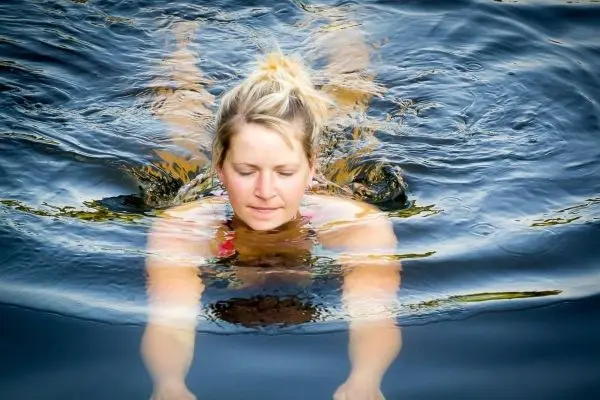 Frau schwimmt mit ausgestreckten Armen in ruhigem Wasser