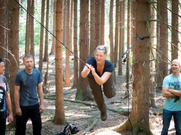 Frau überquert selbstgebaute Seilbrücke zwischen Bäumen im Wald