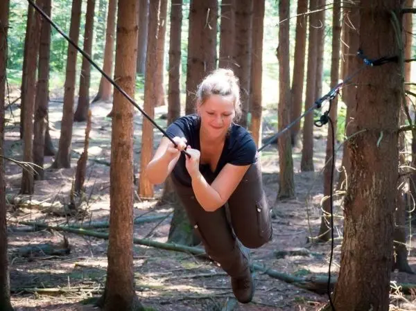 Frau überquert selbstgebaute Seilbrücke zwischen Bäumen im Wald