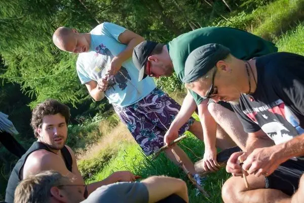 Gruppe arbeitet an Holzstücken im Freien, einige halten Werkzeuge in der Hand