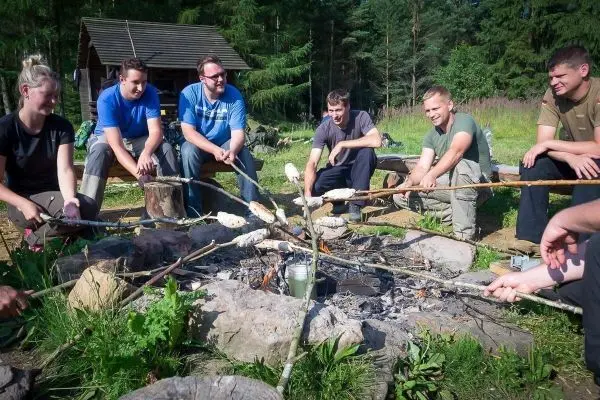 Gruppe sitzt um ein Lagerfeuer und röstet Brot auf langen Stöcken