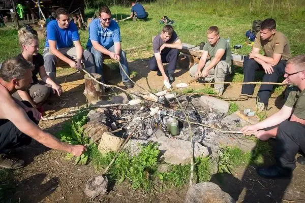 Gruppe sitzt um ein Lagerfeuer und röstet Lebensmittel auf langen Stöcken