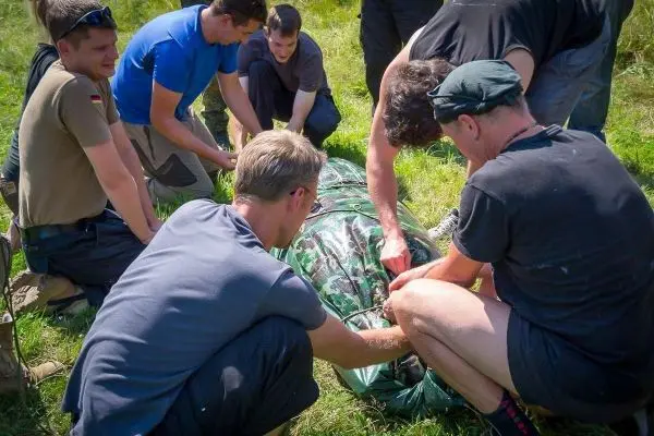 Gruppierung von Personen um eine improvisierte Trage, die mit einem Tuch umwickelt ist