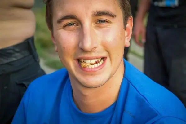 Lächelnder Mann mit einem Snack zwischen den Zähnen trägt ein blaues T-Shirt