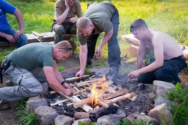 Männer bauen Holzstruktur über kleiner Flamme in Feuerstelle