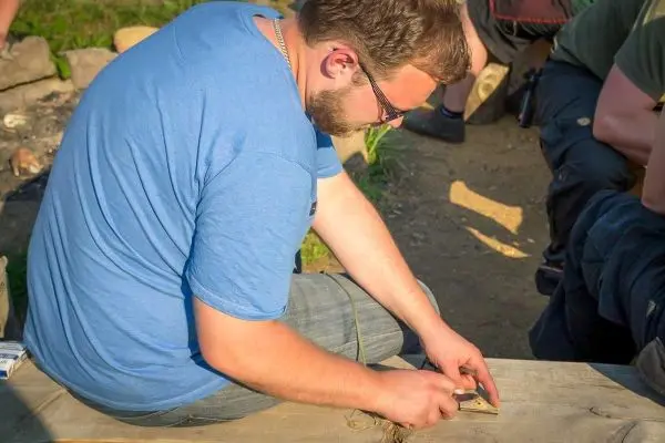 Mann bearbeitet Holzstück mit einem Messer auf einer Holzbank