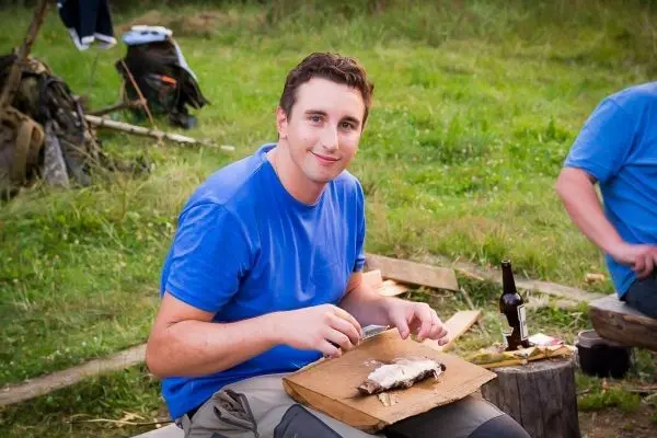 Mann filetiert Fisch auf einem Holzbrett im Freien