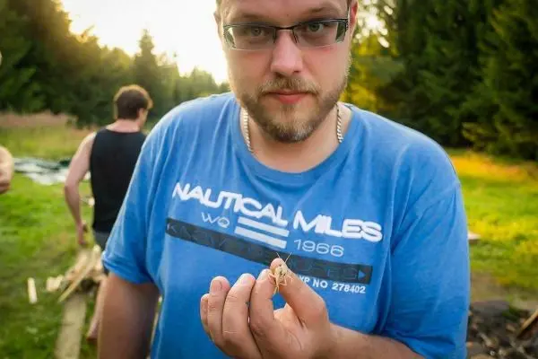 Mann hält ein Insekt in der Hand, im Hintergrund Holz und Bäume sichtbar