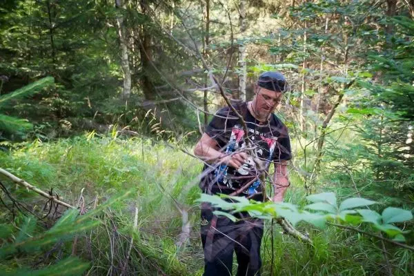 Mann hält ein Werkzeug in der Hand und bewegt sich durch dichtes Unterholz