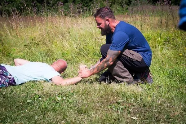 Mann leistet Erste Hilfe bei liegendem Verletzten auf einer Wiese