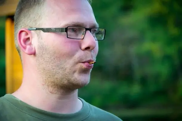 Mann mit Brille bläst Luft aus dem Mund, im Hintergrund grüne Natur