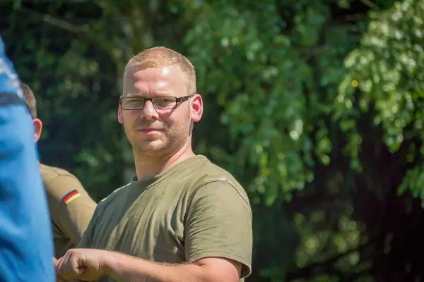 Mann mit Brille und Kurzhaarschnitt steht im Freien und schaut in die Kamera