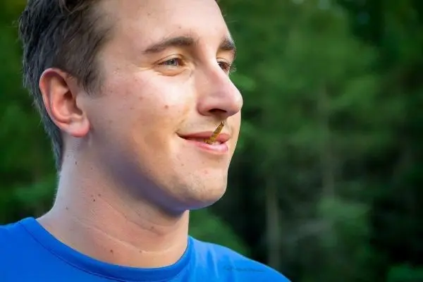 Mann mit einem kleinen Zweig im Mund lächelt in der Natur