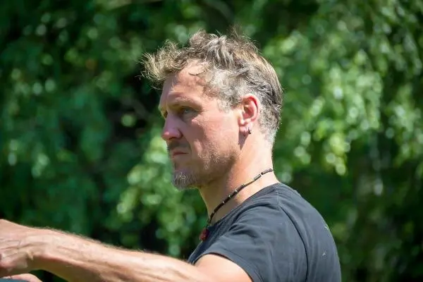 Mann mit kurzen Haaren und Halskette zeigt mit dem Arm in eine Richtung