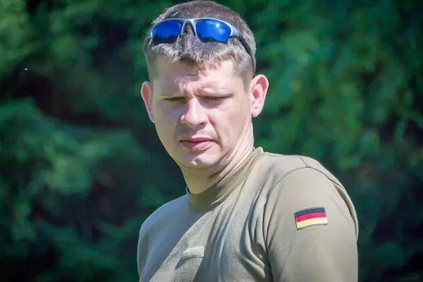 Mann mit Sonnenbrille und olivgrünem Shirt steht im Freien