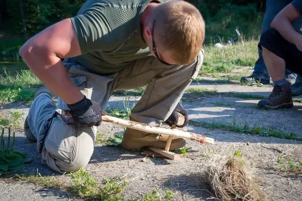 Mann nutzt einen Feuerbohrer, um Zunder zu entzünden