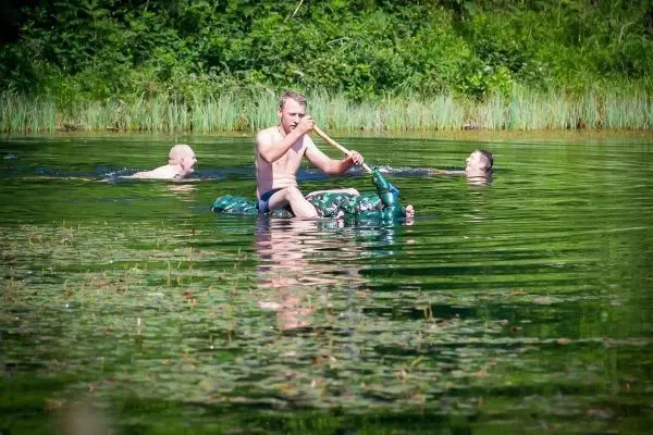Mann paddelt auf einer aufblasbaren Matratze im Wasser, zwei Schwimmer im Hintergrund
