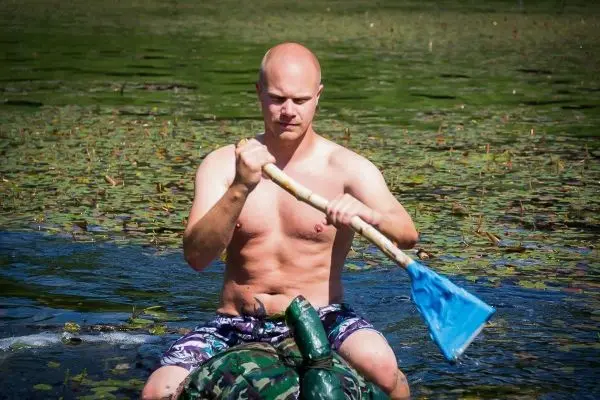 Mann paddelt mit einem blauen Paddel auf einem Wasserfahrzeug im See