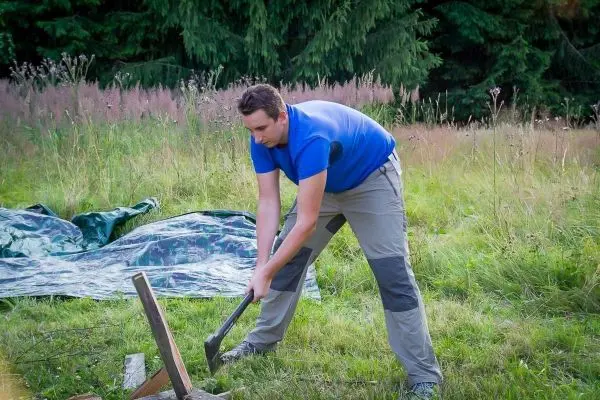 Mann schlägt mit einer Axt auf ein Holzstück im Gras