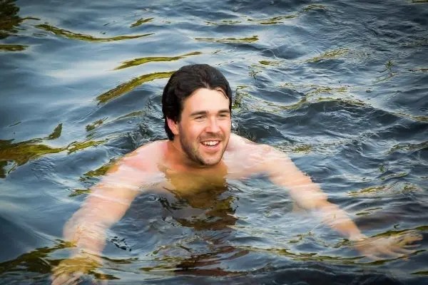 Mann schwimmt lächelnd in einem Gewässer