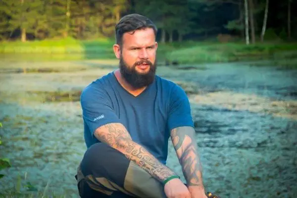 Mann sitzt am Ufer eines Gewässers und betrachtet die Umgebung