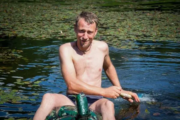 Mann sitzt im Wasser und paddelt mit einem Stock auf einem improvisierten Floß