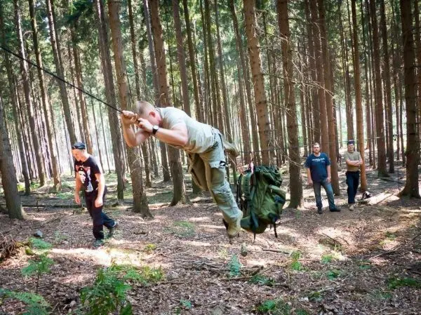 Mann überquert selbstgebaute Seilbrücke mit Rucksack im Wald