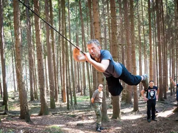 Mann überquert selbstgebaute Seilbrücke zwischen Bäumen im Wald