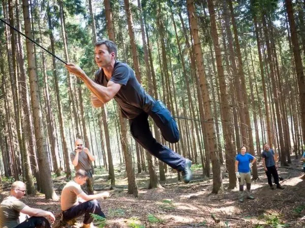 Mann überquert selbstgebaute Seilbrücke zwischen Bäumen im Wald
