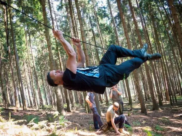 Mann überquert selbstgebaute Seilbrücke zwischen Bäumen im Wald