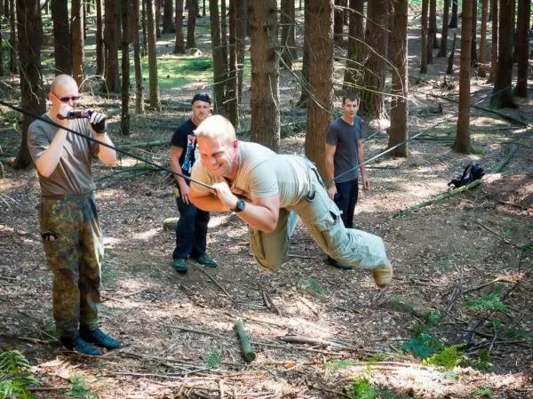 Mann überquert selbstgebaute Seilbrücke zwischen Bäumen, während andere beobachten