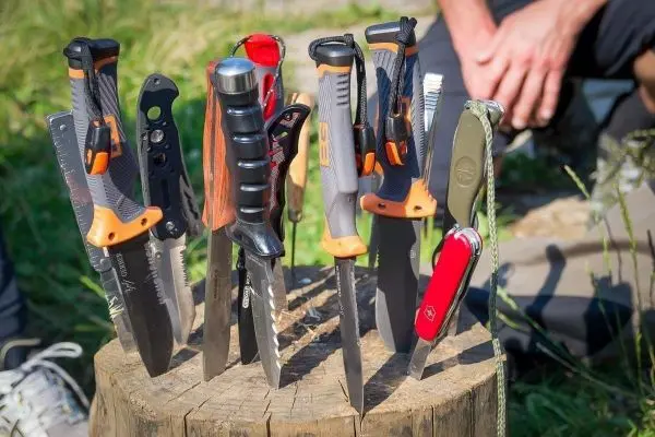 Mehrere Messer stehen auf einem Holzscheit, einige mit farbigen Griffen