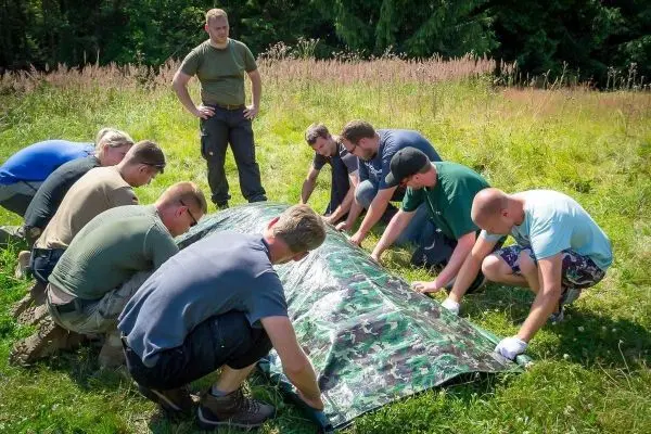 Mehrere Personen ziehen gemeinsam an einer Tarp-Notunterkunft im Freien