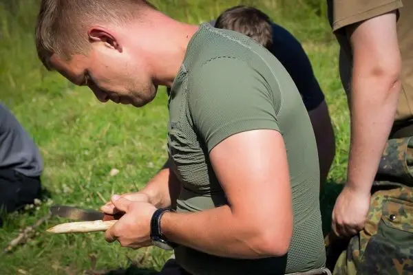 Messer bearbeitet Holzstück in sitzender Position auf Grasfläche