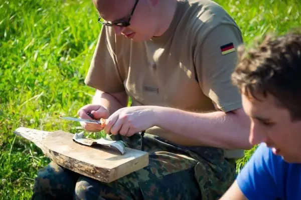 Messer schneidet Zunder auf einem Holzstück im Gras