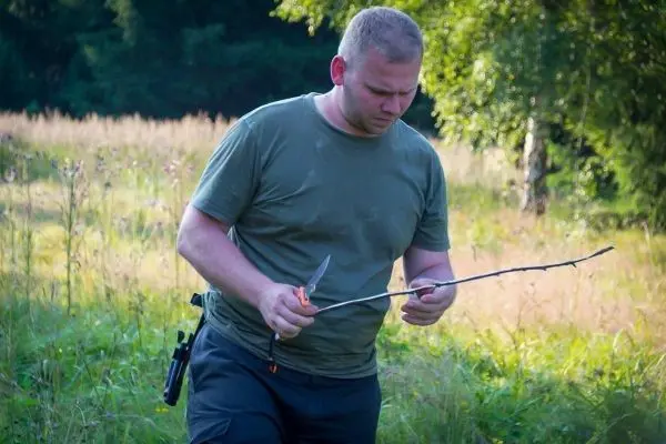 Messer wird an einem Stock gehalten, während im Gras gearbeitet wird