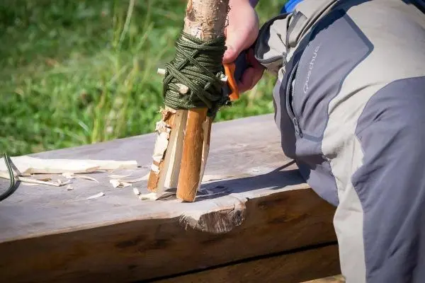 Person bearbeitet Holz mit einem Messer beim Überlebenstraining