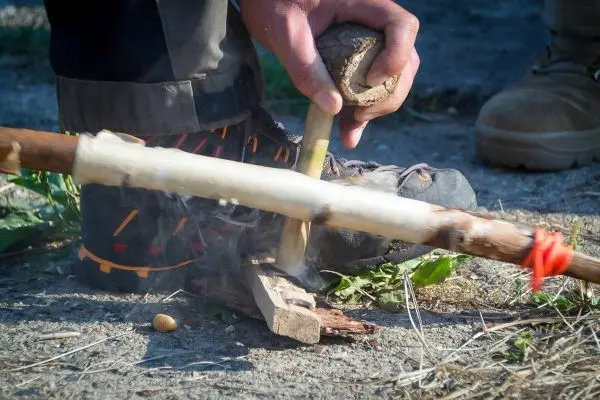 Person bearbeitet Holzstück mit einem Werkzeug beim Feuer machen