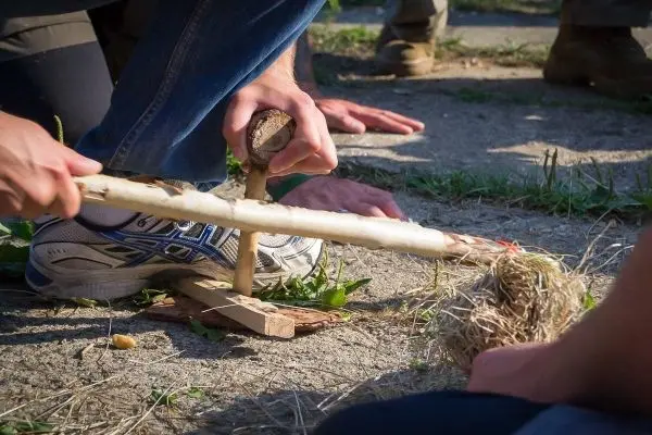 Person erzeugt Feuer mit einem Feuerbohrer beim Survival Training