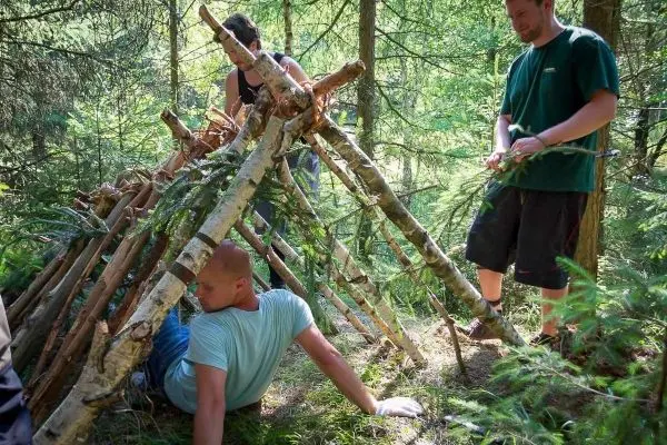 Person sitzt unter einer selbstgebauten Unterkunft aus Ästen und Zweigen