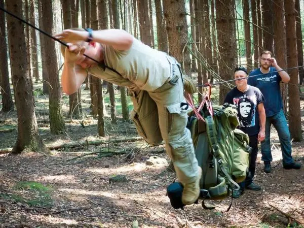Person überquert selbstgebaute Seilbrücke mit Rucksack beim Survival Training