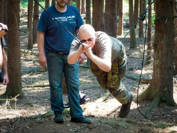 Person überquert selbstgebaute Seilbrücke zwischen Bäumen im Wald