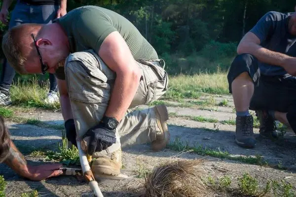 Person zündet mit einem Feuerstahl trockenes Gras an beim Survival Training